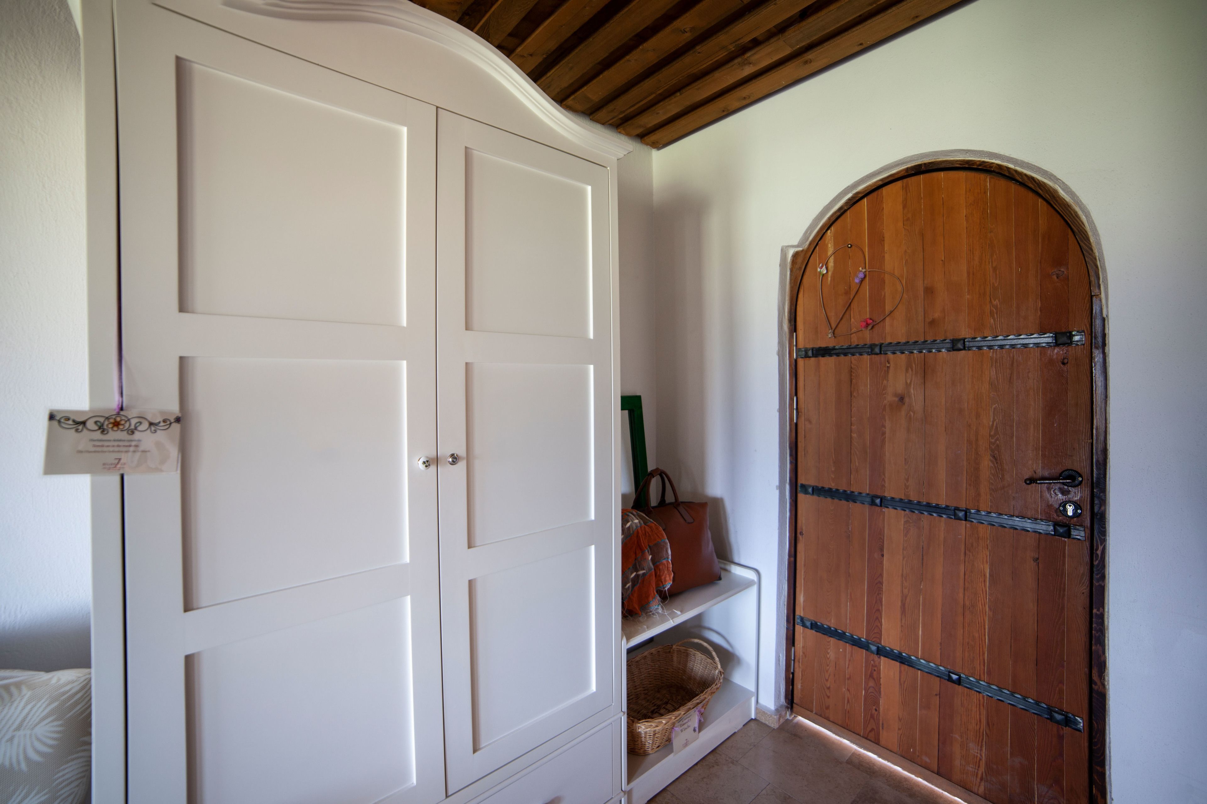 A room with a white wardrobe, a wooden door, and a bench with a bag.