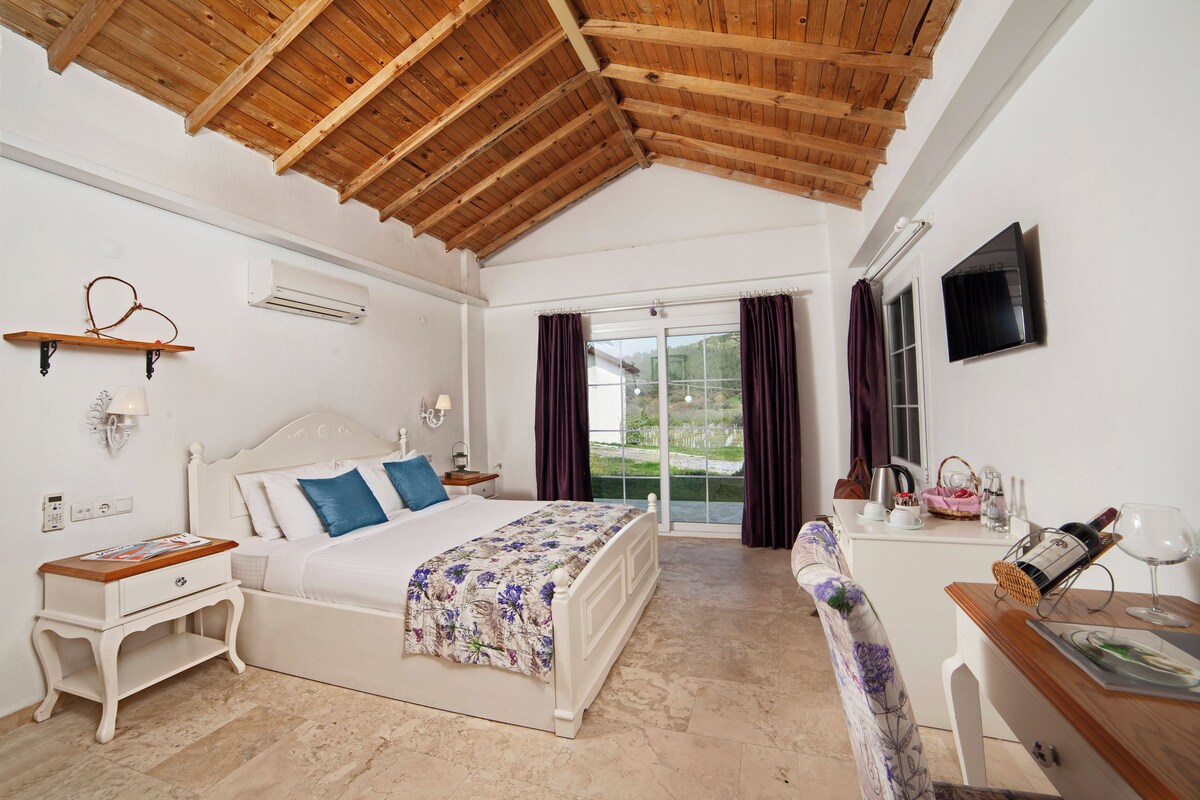 A bedroom with a wooden ceiling, a bed with a floral bedspread, a nightstand, a dresser, and a window with curtains.