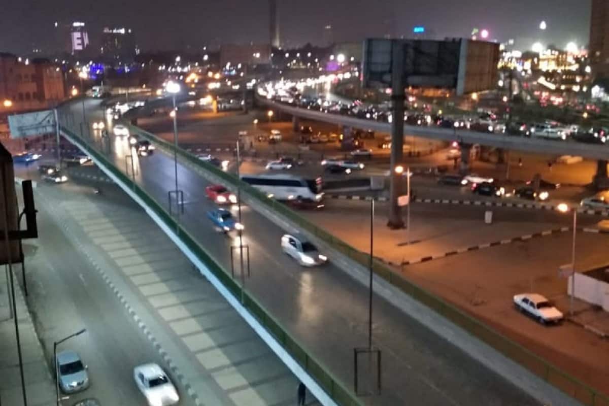 Ein beleuchtetes Stadtbild bei Nacht mit einer mehrspurigen Autobahn und Häusern.