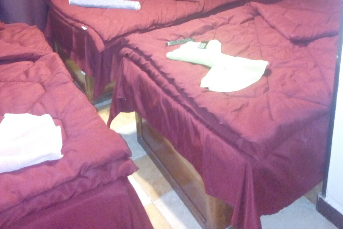 Ein Hotelzimmer mit zwei Betten, beide mit roter Bettwäsche bezogen. Auf einem Bett liegt ein Fernseherlebnis, auf dem anderen ein weißes Tuch.
