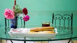 Una mesa de vidrio con una bandeja que contiene pasteles, un vaso de líquido oscuro y un jarrón con flores.