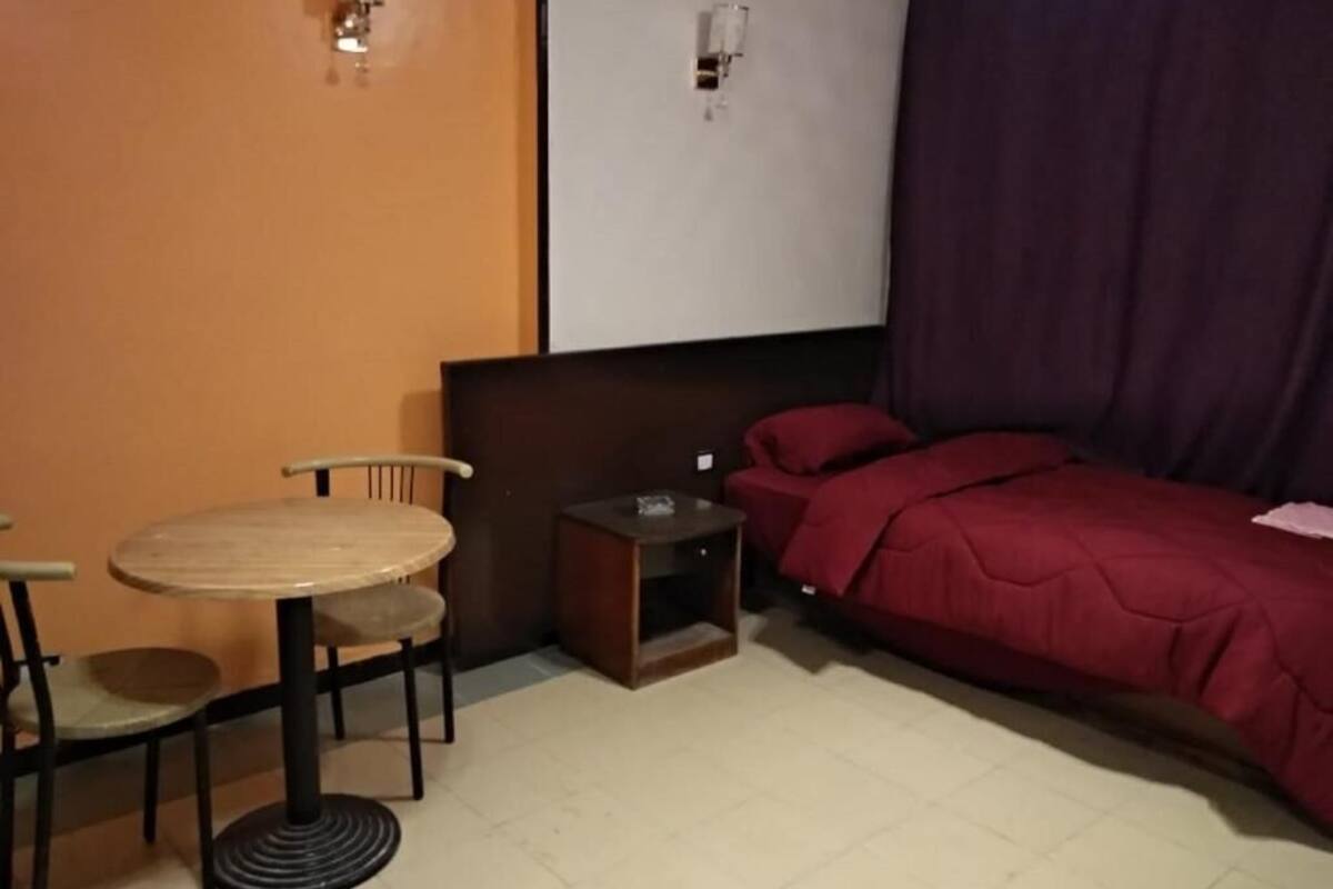 Ein Zimmer mit einem Bett, einem Tisch mit Stühlen, einem kleinen Nachttisch und einer Wandleuchte.