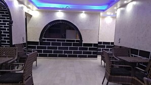 Un restaurante con mobiliario de mimbre, piso de baldosas y pared de ladrillo con un ventanal circular.
