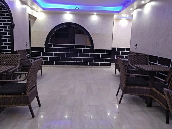 Restaurante com mobiliário de vime, chão de azulejos e parede de tijolos com uma janela redonda.