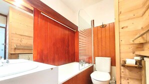 Un baño estilo cabaña de madera con lavamanos, espejo y retrete blancos.