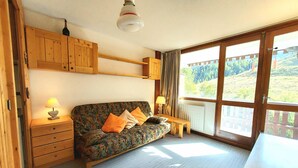Una habitación acogedora con un sofá de madera, dos lámparas, una mesita y un amplio ventanal con vistas a una zona boscosa.