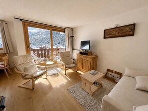 A cozy room with a large window, a television, a wooden cabinet, and a bed.