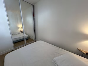 Ein Schlafzimmer mit einem Bett, einem Nachttisch mit Lampe und einer Schiebetür, die in einen anderen Raum führt.