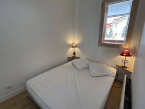 A small, single-bed room with a window, two bedside lamps, and a radiator.