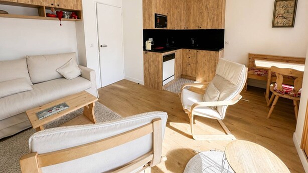 Een compacte leefruimte met een bank, een stoel, een klein tafeltje en een kitchenette.