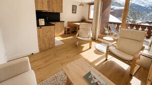 Een gezellige woonkamer met een houten vloer, een bank, een salontafel en een balkon met uitzicht op besneeuwde bergen.