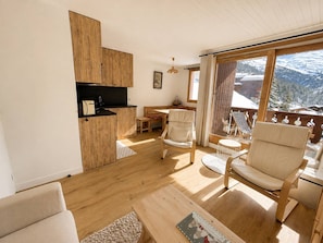 Ein gemütliches Wohnzimmer mit Holzboden, einer Couch, einem Couchtisch und einem Balkon mit Blick auf schneebedeckte Berge.