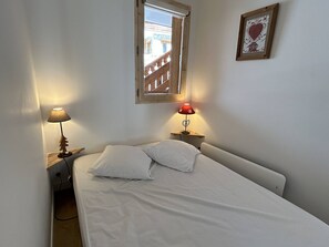 Un dormitorio con cama, dos lámparas de noche, una ventana y un cuadro en la pared.