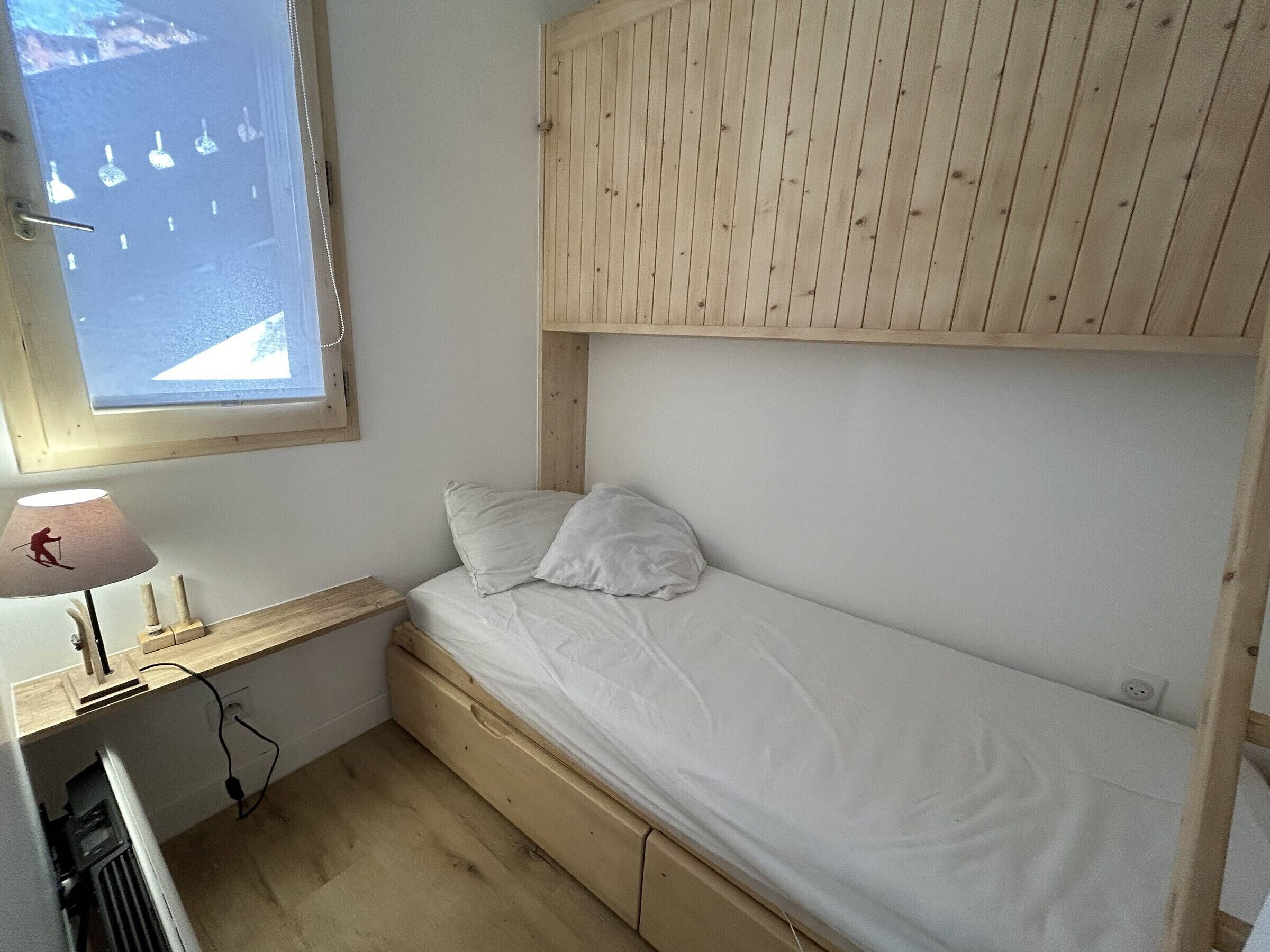 Une chambre avec un lit superposé, une fenêtre, un bureau avec une lampe et un radiateur.