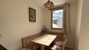 A cozy room with a wooden bench, a small table, and a window with a view of snow-covered mountains.
