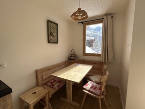 A cozy room with a wooden bench, a small table, and a window with a view of snow-covered mountains.