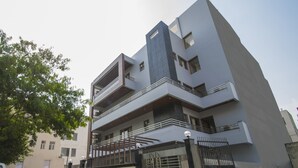 Un edificio moderno de varios pisos con techo plano, balcones y entrada protegida por una reja.