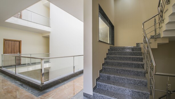 Un interior amplio con balcón de cristal, suelo de mármol y escalera con barandillas metálicas.