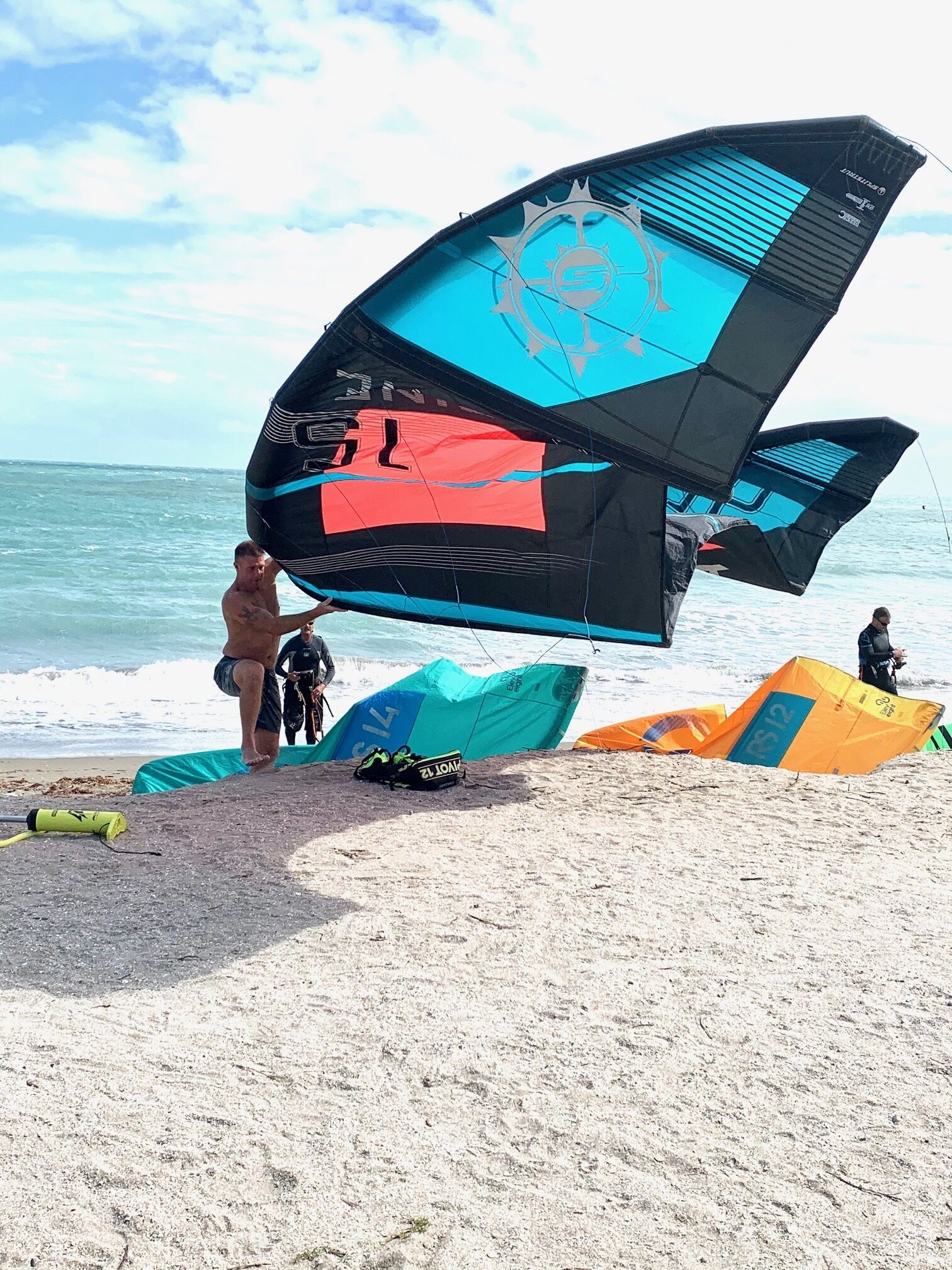 A beach with multiple kites and a person handling a kite.
