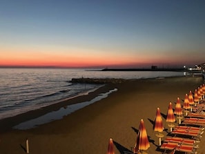 Ein Strand mit Reihen von Liegestühlen und Sonnenschirmen, ruhigem Meer und einem Abendhimmel.