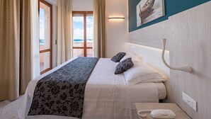 A hotel room with a bed, a bedside table with a phone, and a view of the sea through a glass door.