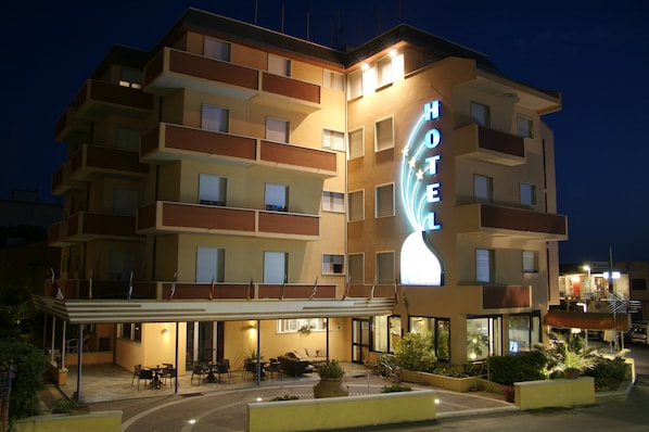 Ein mehrstöckiges Hotel mit auffälligem Neonzeichen, Außenbereich mit Sitzgelegenheiten und einem überdachten Eingang.