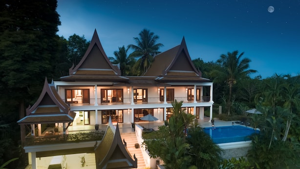 Un edificio grande de varios pisos con un estilo arquitectónico tradicional, que cuenta con una piscina y exuberantes alrededores tropicales.