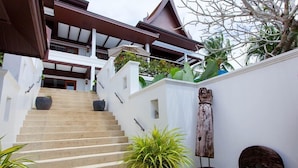 Una escalera conduce a un edificio moderno de estilo arquitectónico tradicional, rodeado de vegetación y elementos decorativos.
