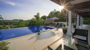 Una piscina infinita con vistas a una vegetación exuberante y una casa tradicional al fondo.