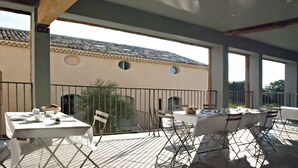 An outdoor dining area with tables and chairs, a tiled roof, and a view of a building with circular windows. - Chartreuse de Mougeres (Caux)
