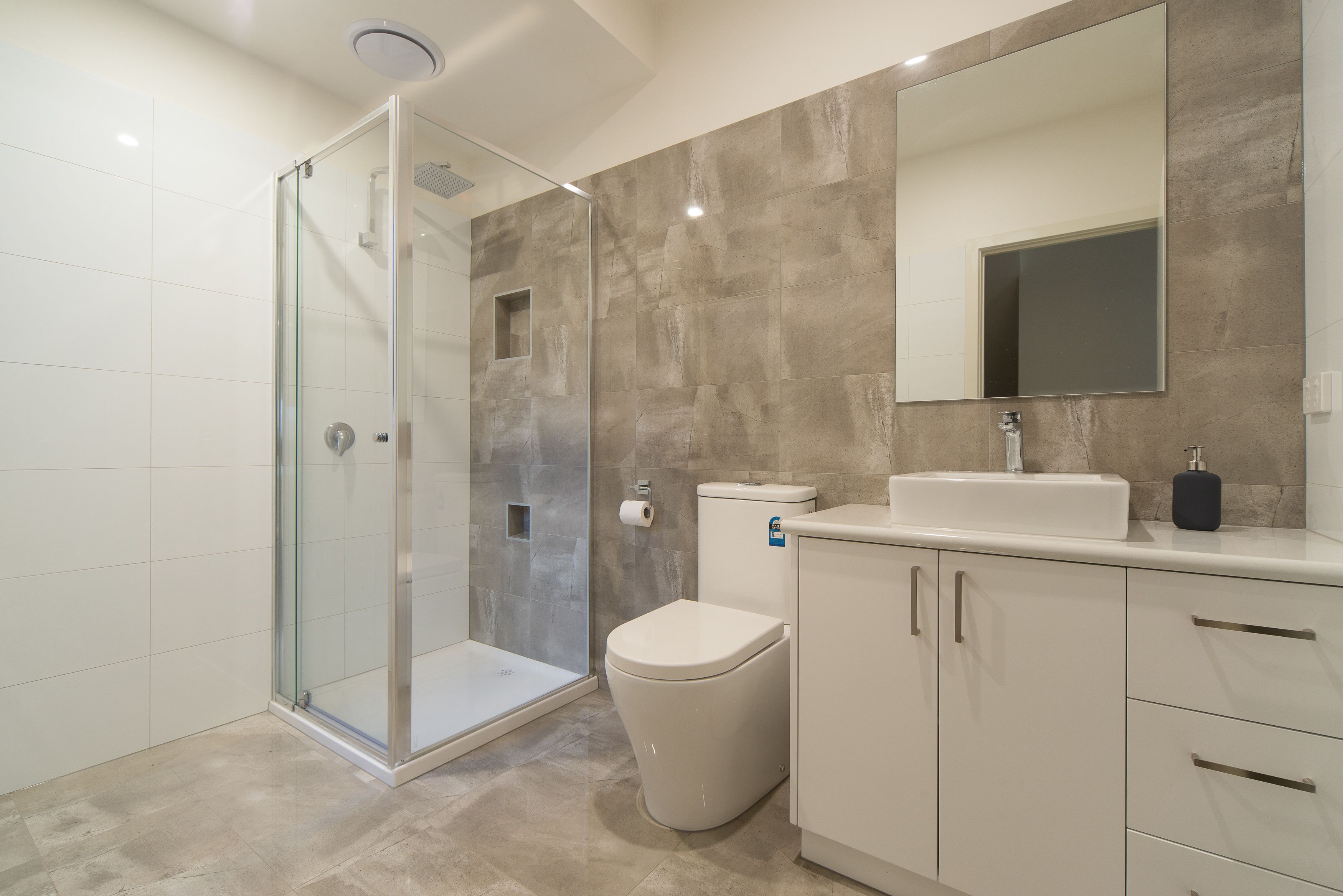 Un baño moderno con ducha envuelta en vidrio, un inodoro y un lavabo con espejo arriba.