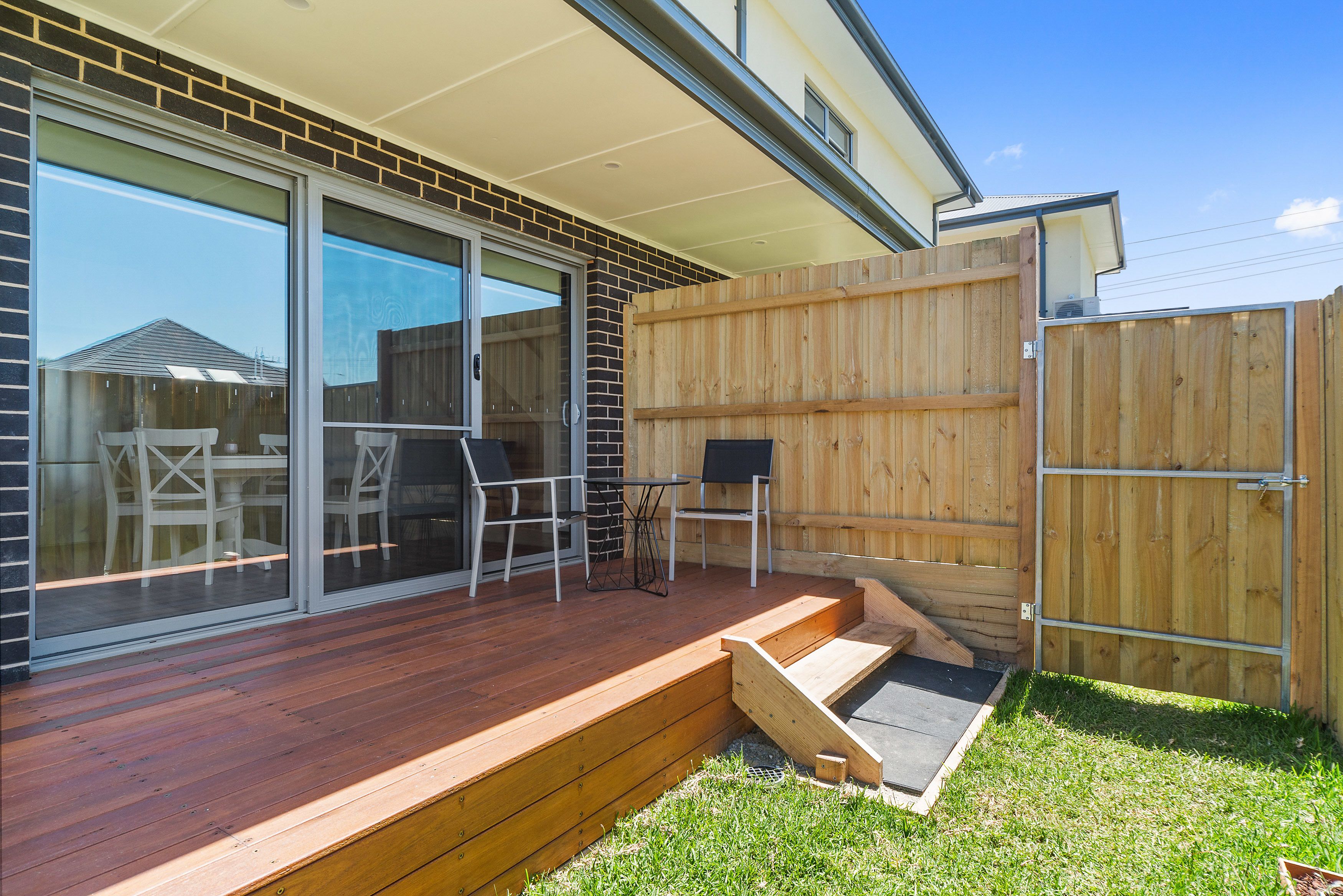 Eine überdachte Terrasse mit Holzdeck, einer Glastürfront und einer kleinen Sitzgruppe mit Stühlen und Tisch.