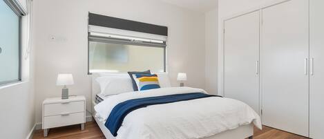 Een moderne slaapkamer met een bed, nachtkastjes, een raam met jaloezieën, een kledingkast en een airconditioning.