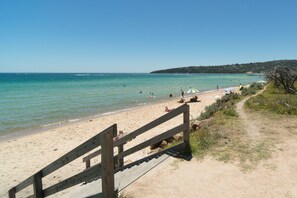 A beach with a wooden walkway leading to the water, a sandy shore, and a few umbrellas and people. - Rosewater Dromana (Dromana)