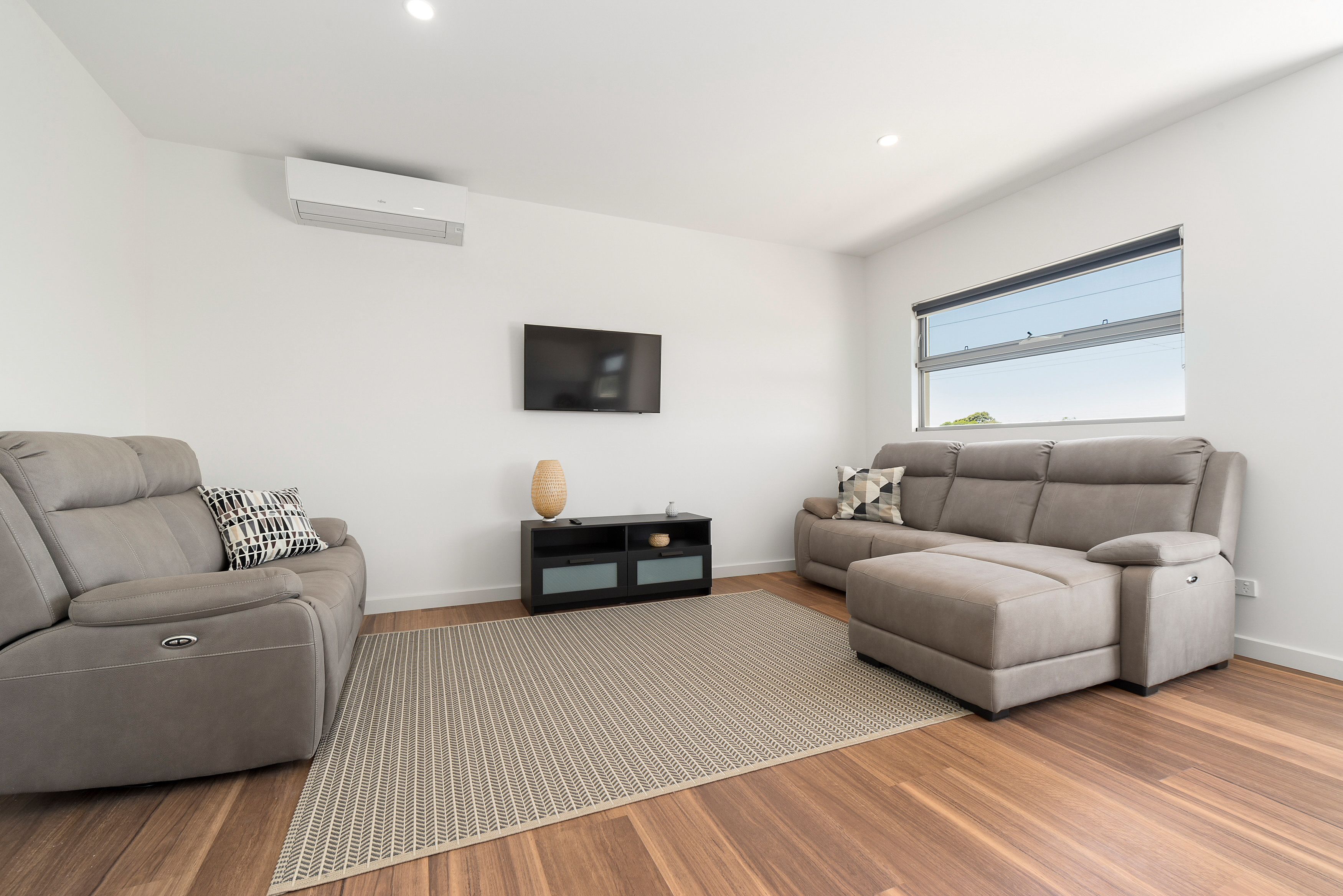 Un salon moderne avec deux canapés gris, un meuble de rangement noir pour les appareils électroniques et une grande fenêtre offrant une belle vue.