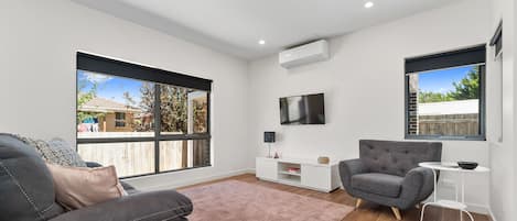 Una sala de estar moderna con un ventanal grande, un sofá gris, una mesita auxiliar blanca y un sillón gris.