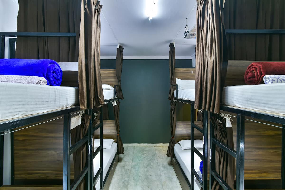 Una habitación estrecha con literas, piso de madera y pared verde.