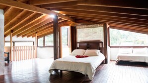 Une chambre avec un plafond en bois, un lit recouvert de draps blancs et une vue dégagée sur l’extérieur grâce à de grandes fenêtres.