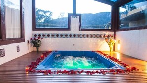Un bain à remous agrémenté de pétales de rose et de bougies, installé dans une pièce offrant une vue sur les collines.
