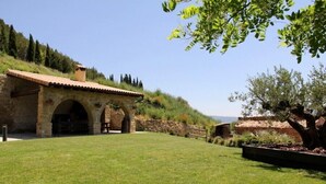 A stone building with arches and a tiled roof, surrounded by a grassy area and trees. - Casa Rural Fernandoegea (Ezprogui)