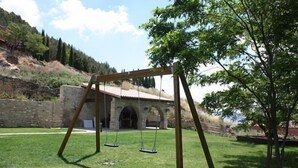 A wooden swing set in a grassy area with a stone building in the background. - Casa Rural Fernandoegea (Ezprogui)