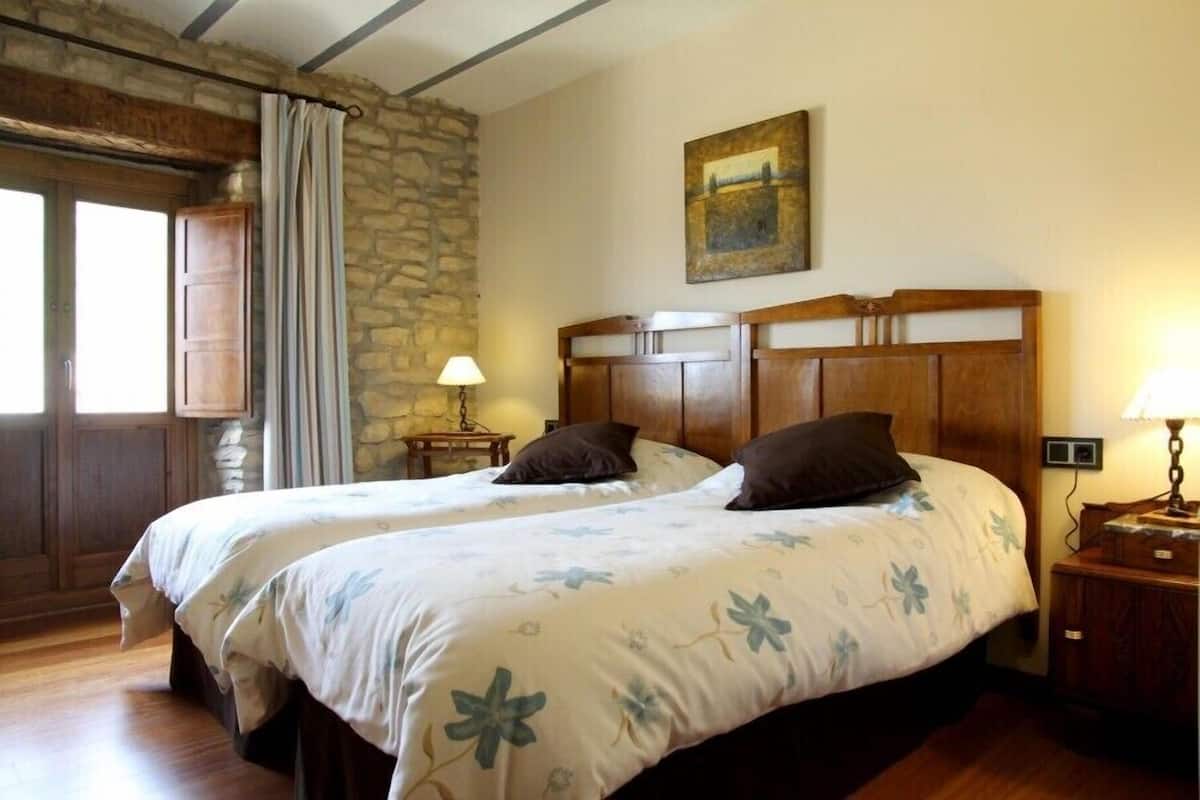 Ein Doppelbett mit floralem Bettzeug, eine Steinwand und ein Bild an der Wand.