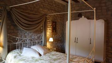 Ein Himmelbett mit Steinwand im Hintergrund, ein weißer Kleiderschrank und ein Nachttisch mit Lampe.