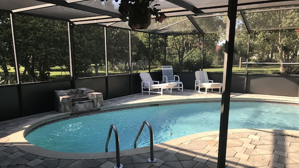 A covered swimming pool with a stone-tiled deck, lounge chairs, and a view of a grassy area with trees. - 3 bedroom Pool home. Quiet Neighbourhood (Spring hill)