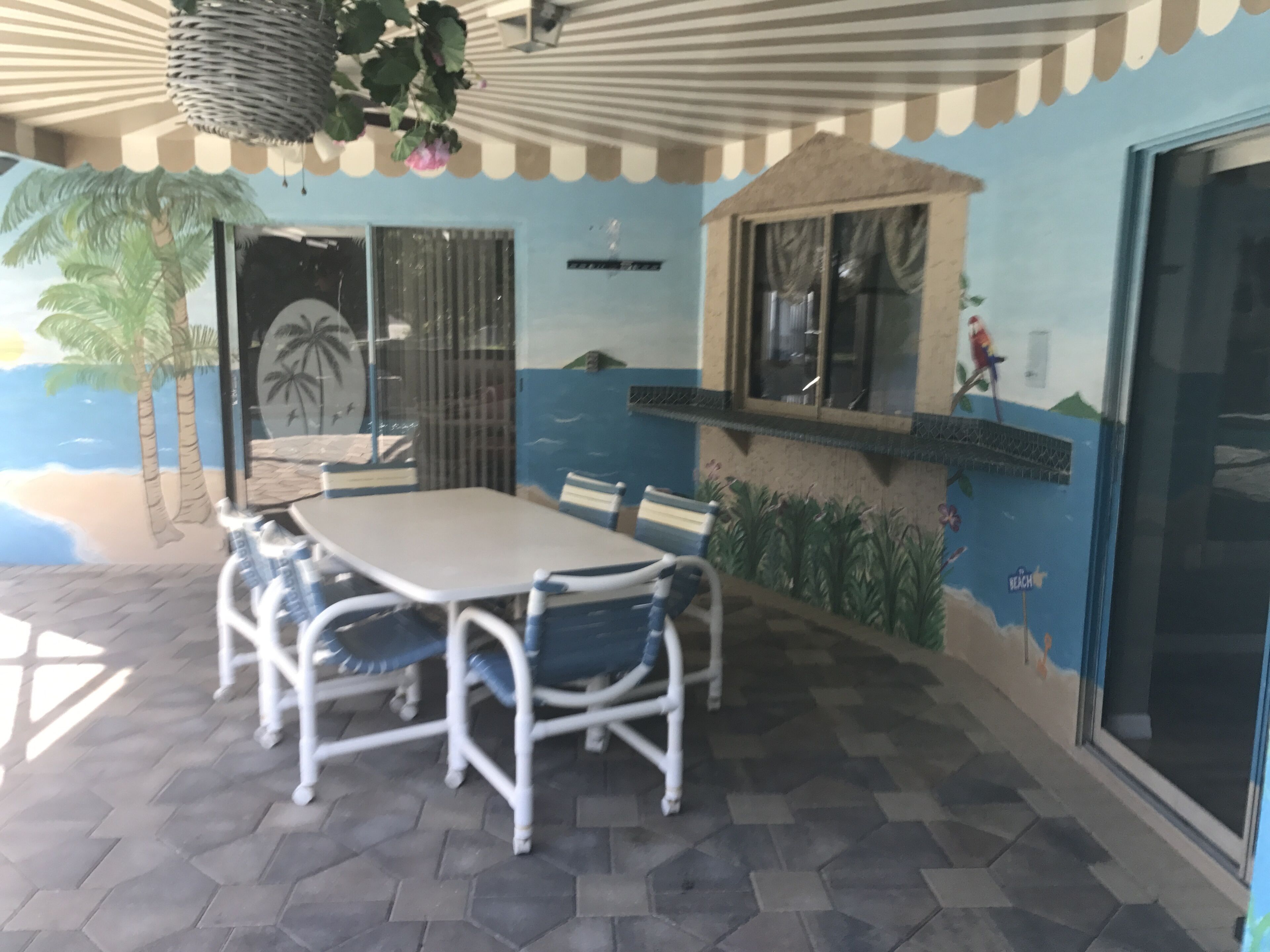 A dining area with a table and chairs, a hanging plant, and a mural of a beach scene.