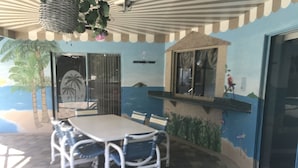 A dining area with a table and chairs, a hanging plant, and a mural of a beach scene. - 3 bedroom Pool home. Quiet Neighbourhood (Spring hill)