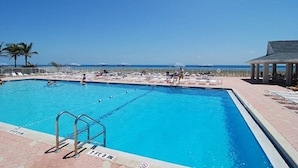 Piscina retangular com água azul cristalina, cercada por um deck ladrilhado e cadeiras de descanso.