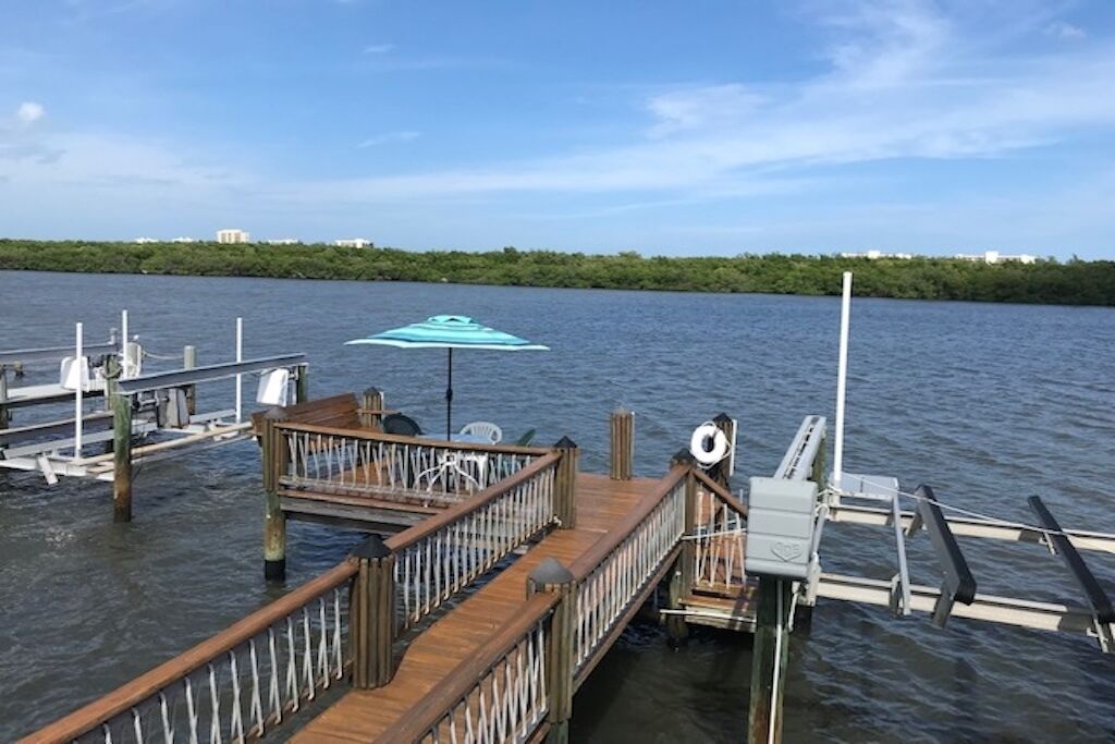 A wooden dock extending into calm water with a lifebuoy and a blue umbrella.