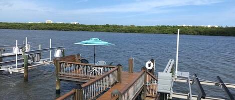 A wooden dock extending into calm water with a lifebuoy and a blue umbrella.