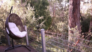 A wicker chair with a cushion in a forested area, surrounded by a wooden fence. - Heavenly Retreat - King bed, luxury spa, undercover parking! (Halls Gap)
